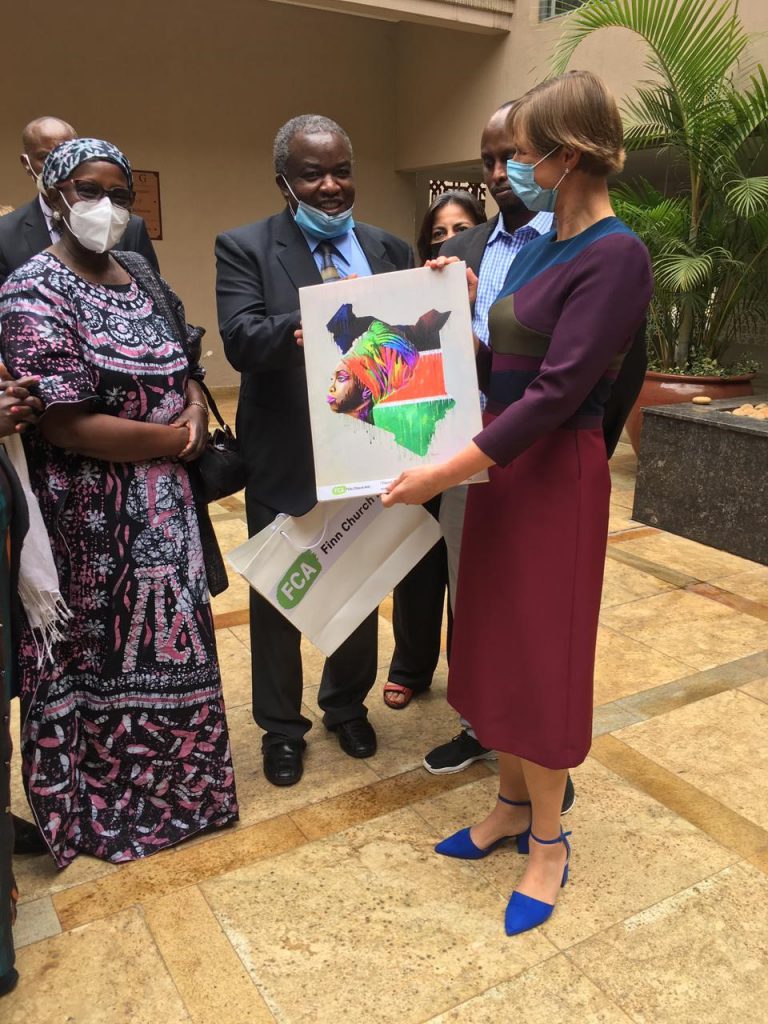Woman on the right, former President of Estonia, Ms. Kersti Kaljulaid receiving an art work from a group of people including FCA Country director John Bongei.