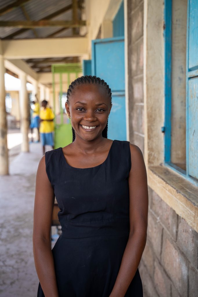 Samantha Mwangome, standing beside a classroom, smiling